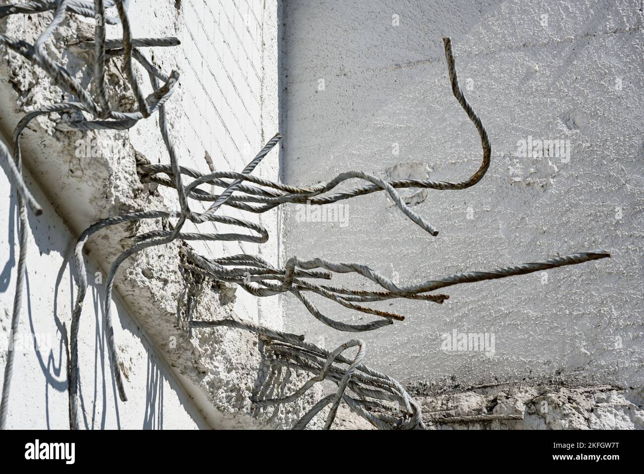 Rebars from iron stick out of a bright concrete wall after demolition, abstract grunge concept for decay or architecture and building themes, copy spa Stock Photo