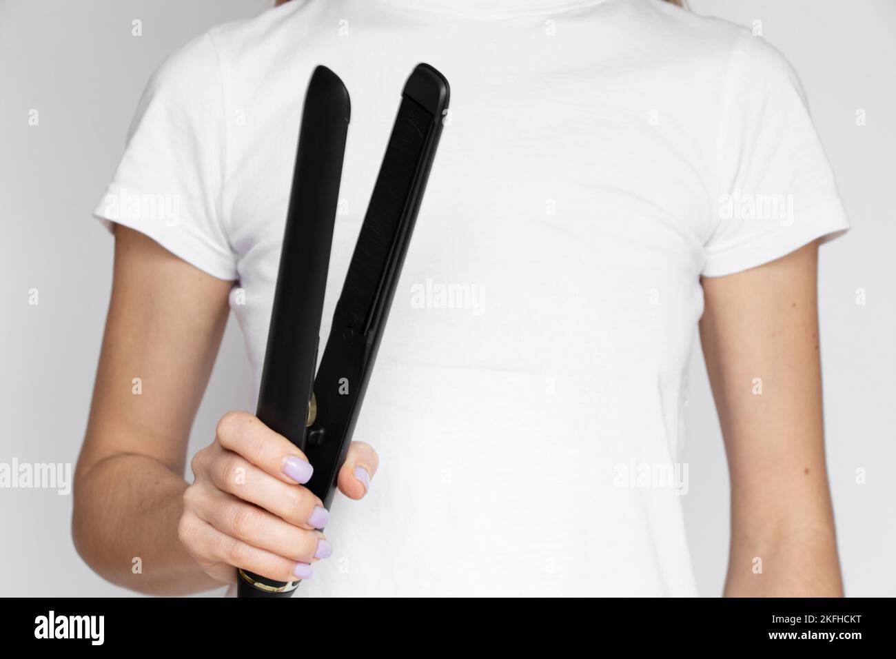 The girl straightens her hair with straightening tongs on a white