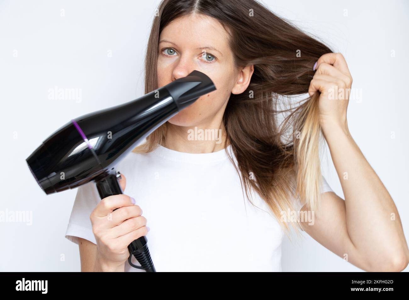 The girl dries her hair with a hairdryer on a white background, hair