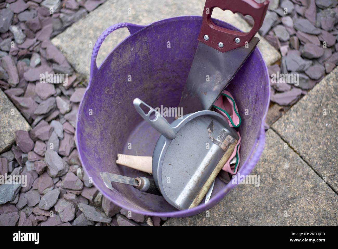 Purple plastic bucket filled with workman's tools. Saw, brush and pan Stock Photo