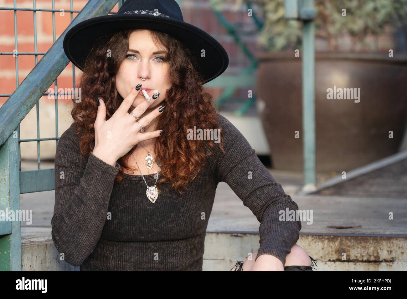 a half-body natural portrait of a woman in a black hat smoking a cigarette Stock Photo
