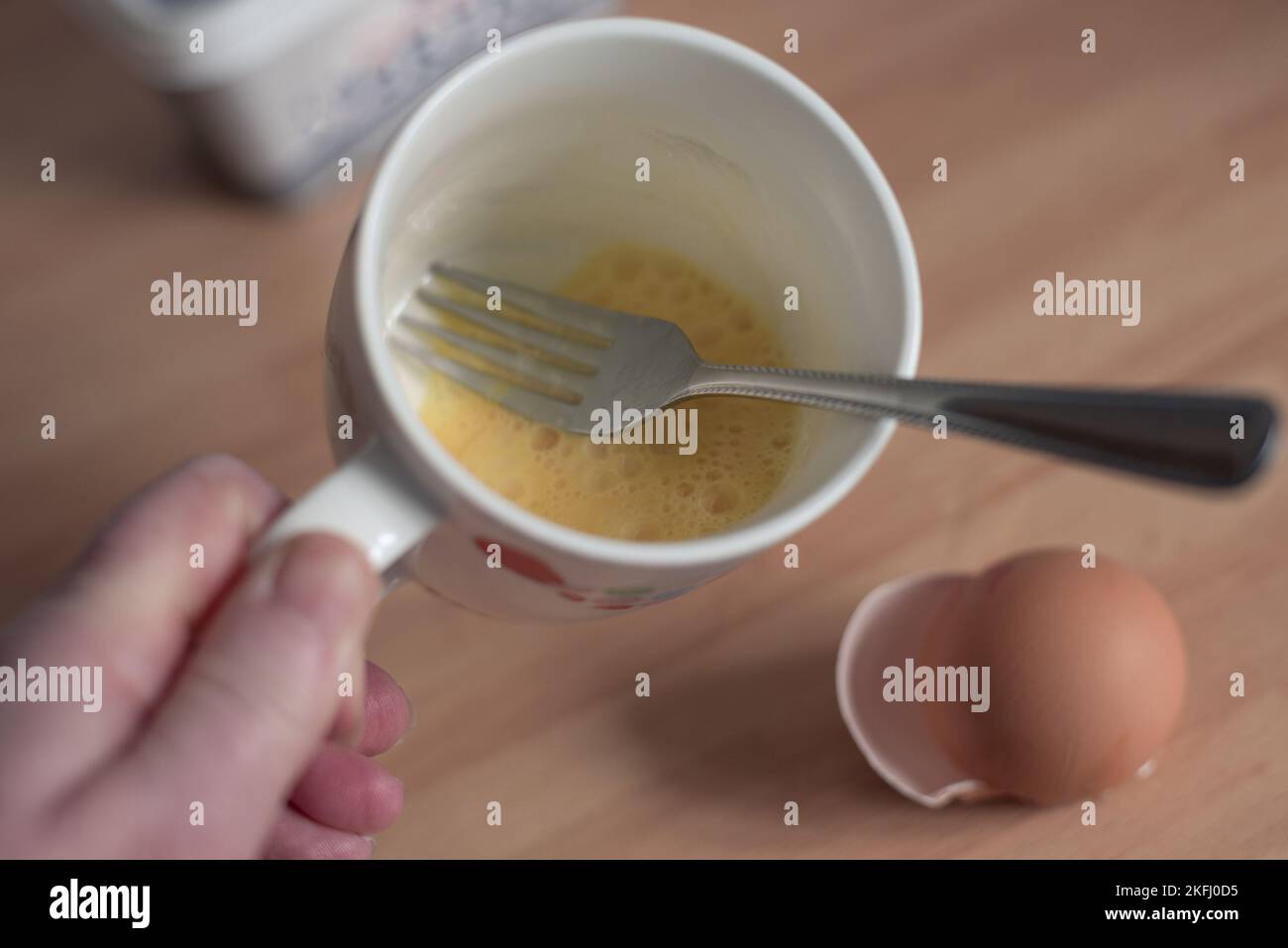 Egg in a cup with a fork to whisk the egg. cracked egg shell on the work top. Stock Photo