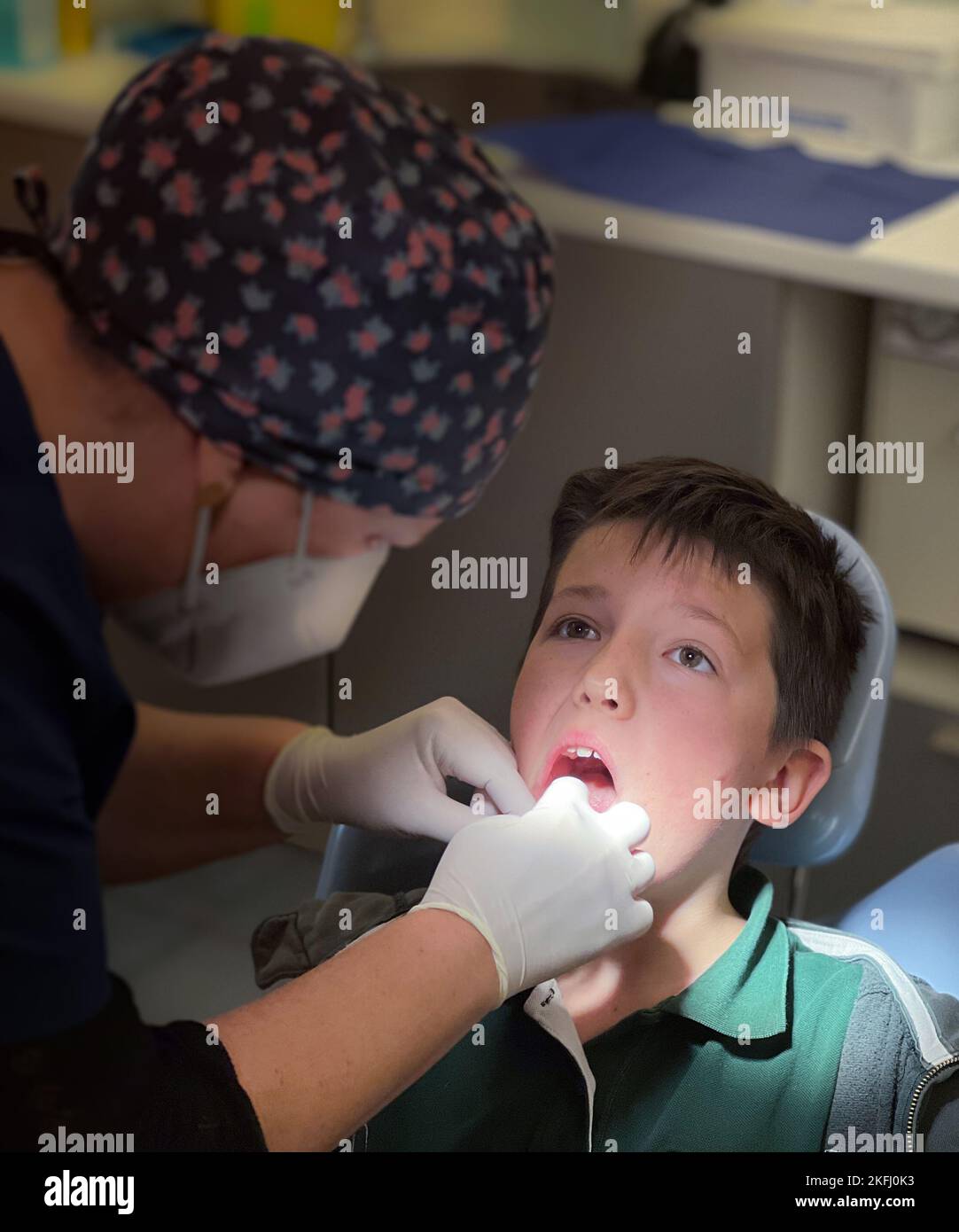 Female dentist wearing floral cap examining adolescent boy's teeth