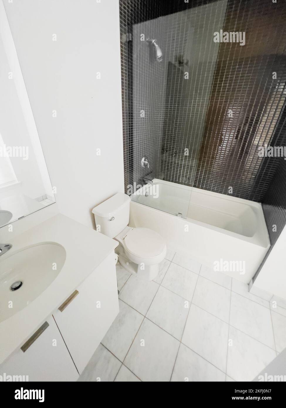 White bathtub by toilet seat and sink against mosaic wall in clean modern bathroom. Stock Photo