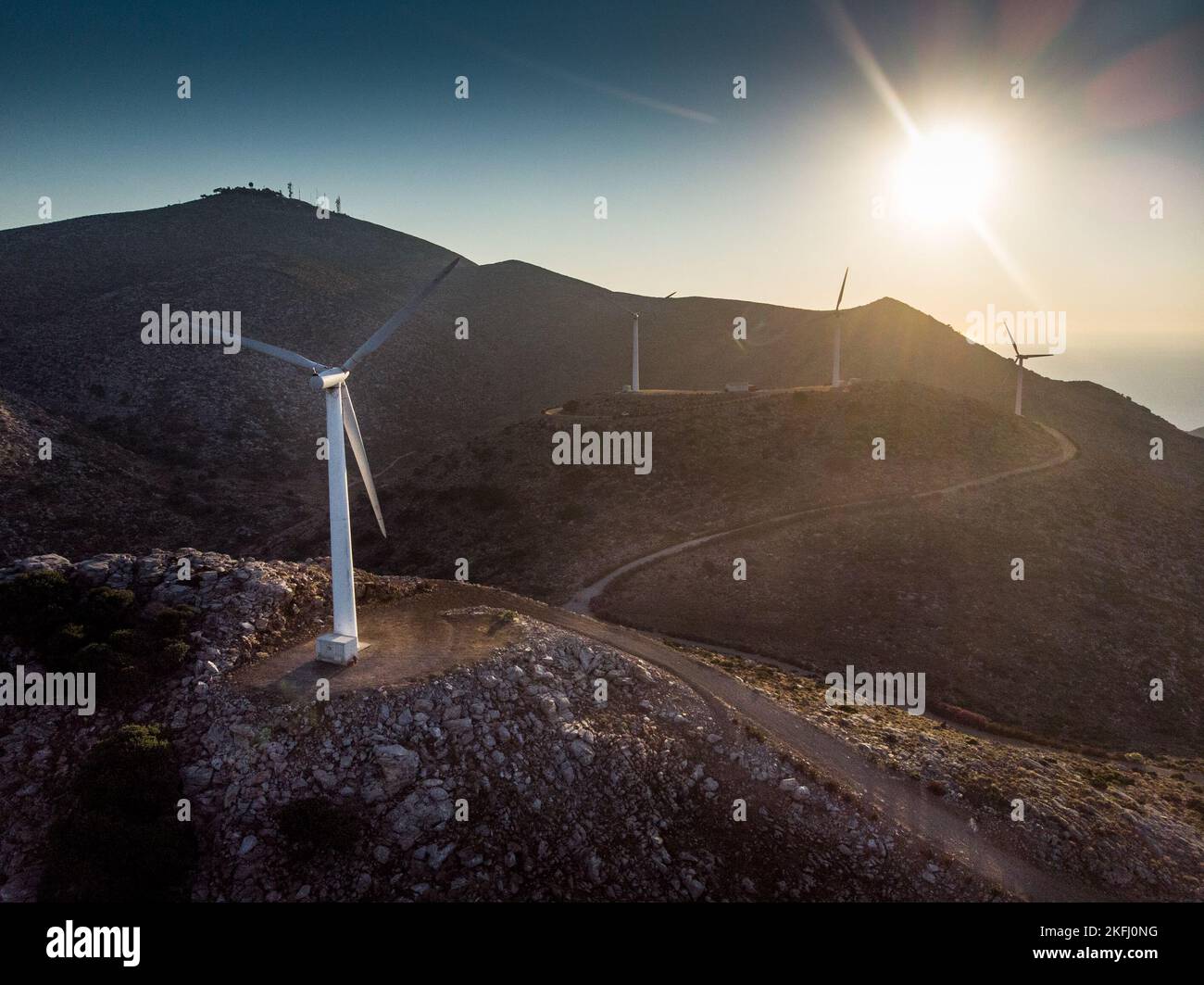 Wind turbines on landscape and Idyllic shot of silhouette mountain range against bright sun in sky during sunset Stock Photo