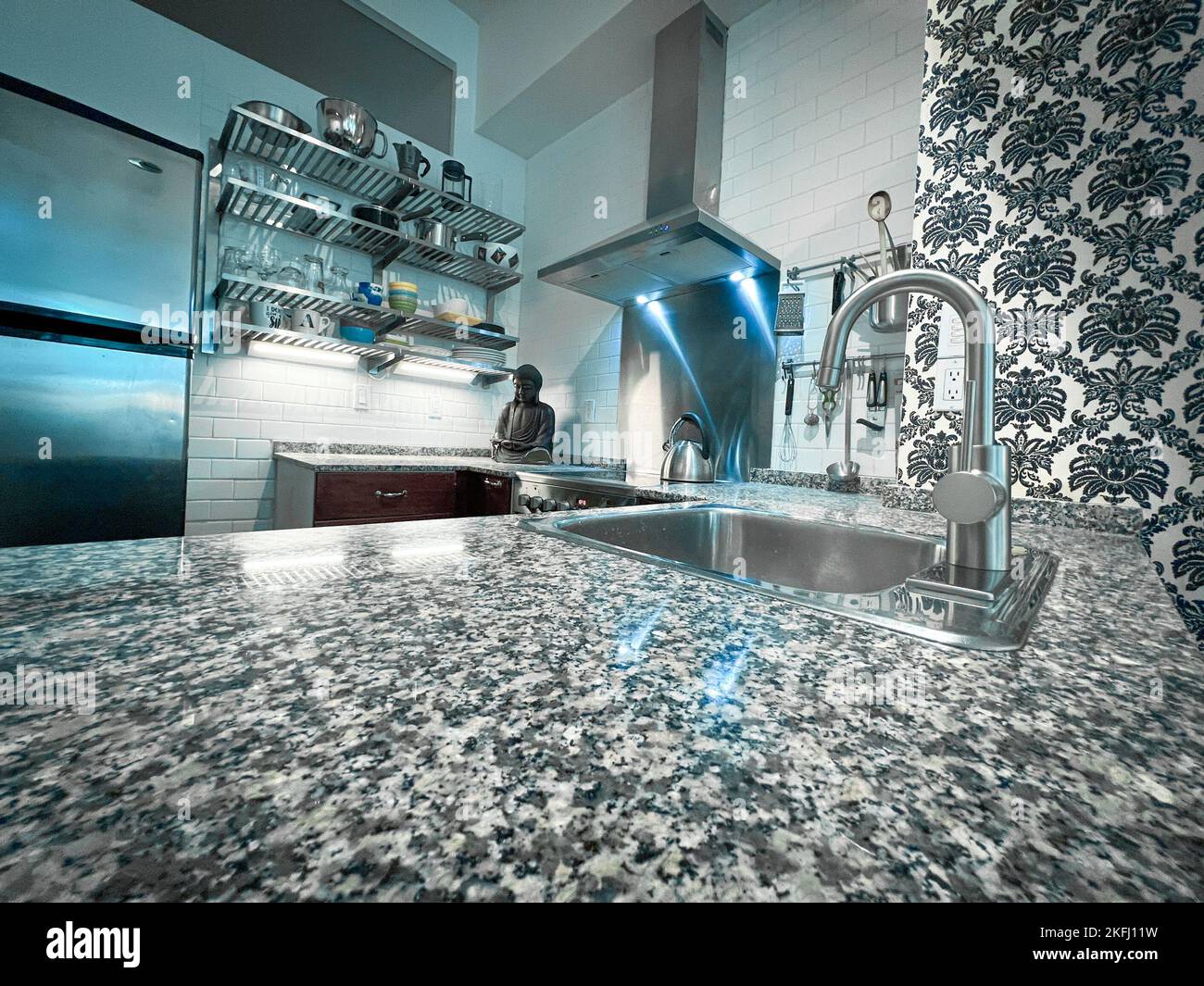 Steel faucet with sink on kitchen island and buddha figurine with illuminated range hood in modern kitchen at home Stock Photo