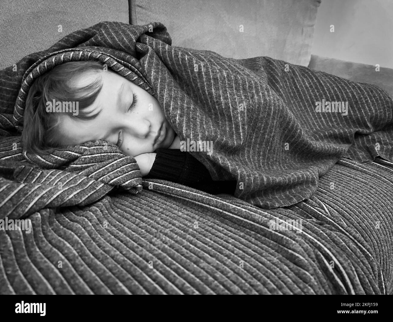 Cute Caucasian boy covered with striped blanket sleeping comfortably on sofa in living room at home Stock Photo