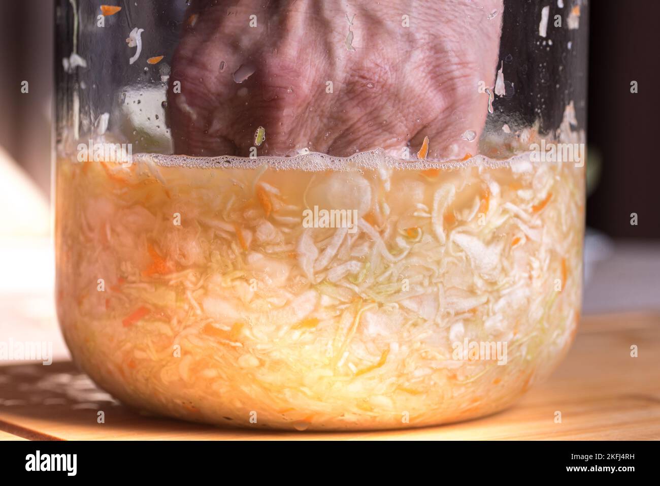 Man tamping down homemade sauerkraut with hand in jar.. Finely chopped