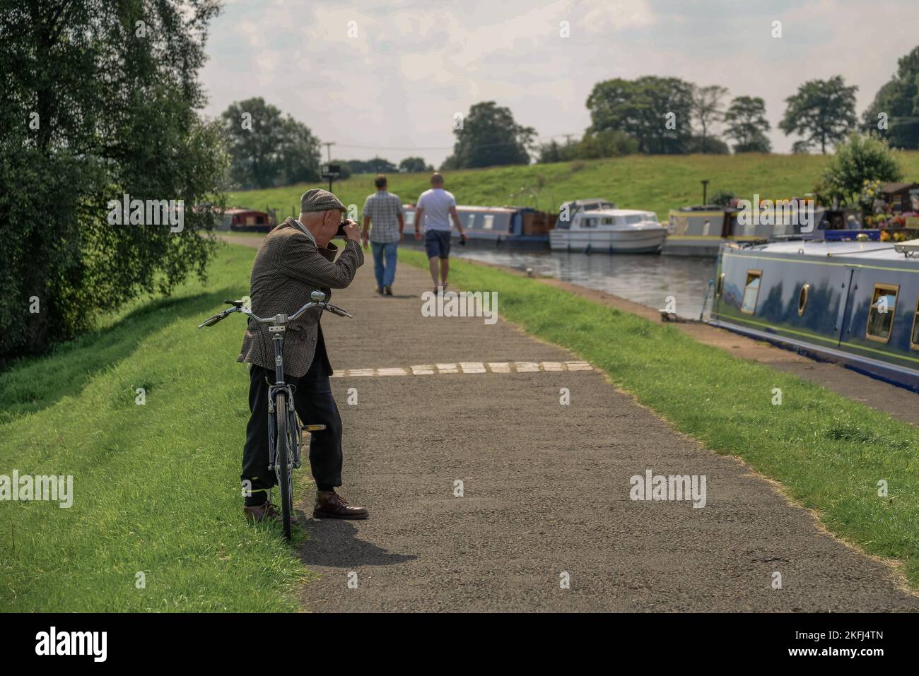 Old man riding a bicycle wearing a flat cap. Stopped to take photographs along the canal. Taken along the Leeds Liverpool Canal at Barrowford Stock Photo