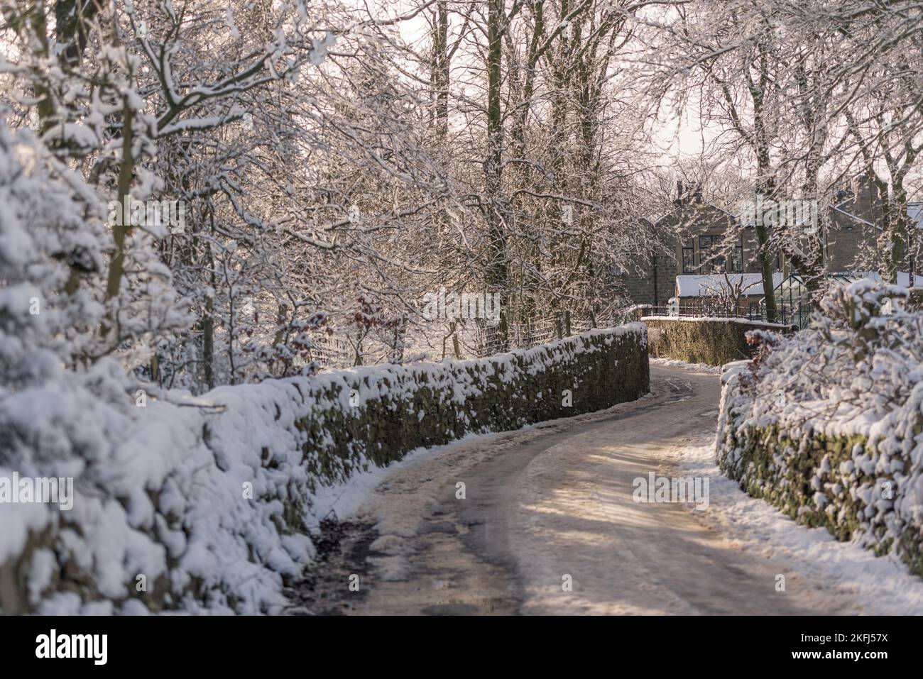 Snow covered English country lane with stone walls winding through the