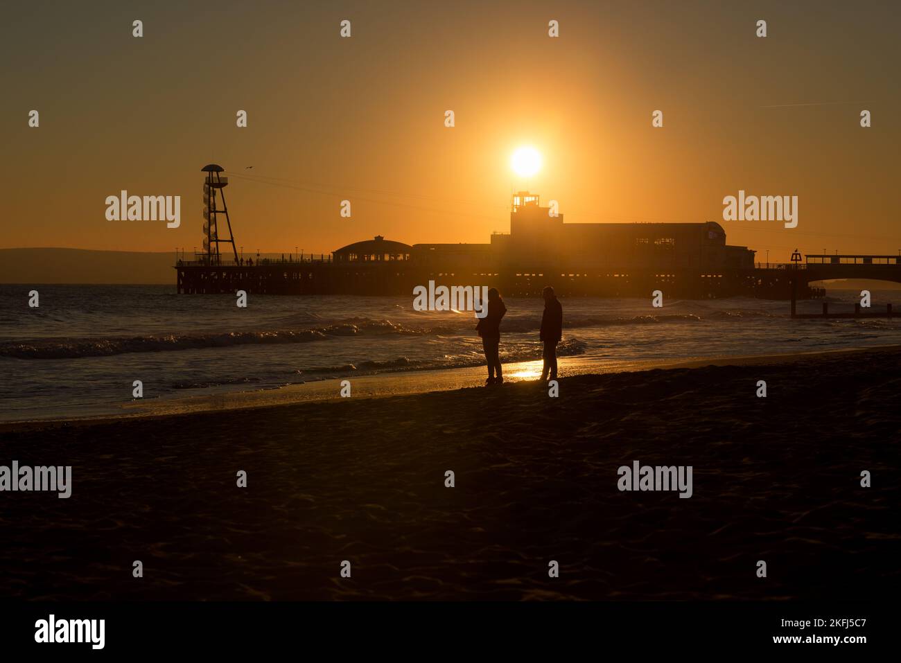 Silhouette of a couple on the beach at sunset. Pier in the background ...