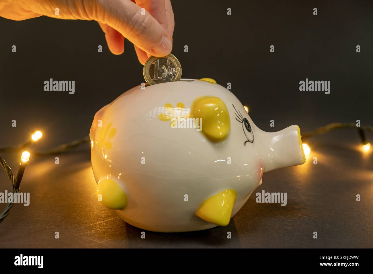 Putting one euro coin in a piggy bank, on a dark background with small led lights. Concept of saving money. copy space. Stock Photo