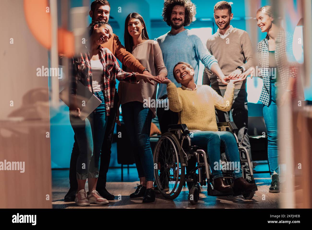 Businesswoman in a wheelchair on break in a modern office with her team in the background Stock Photo