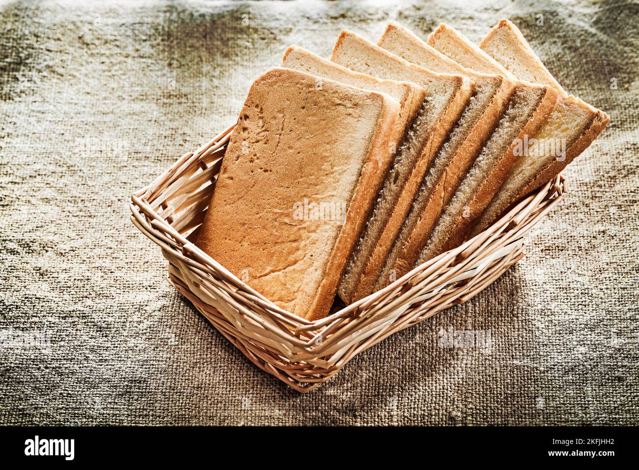 Wicker basket sliced bread on vintage burlap background. Stock Photo