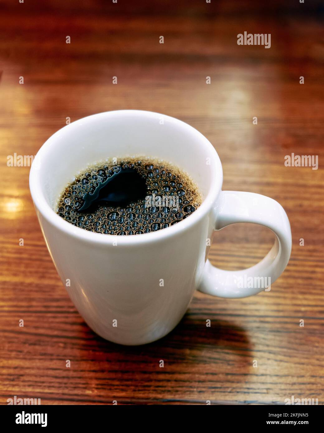 Large white ceramic coffee cup or mug with hot black coffee on a restaurant table. Stock Photo