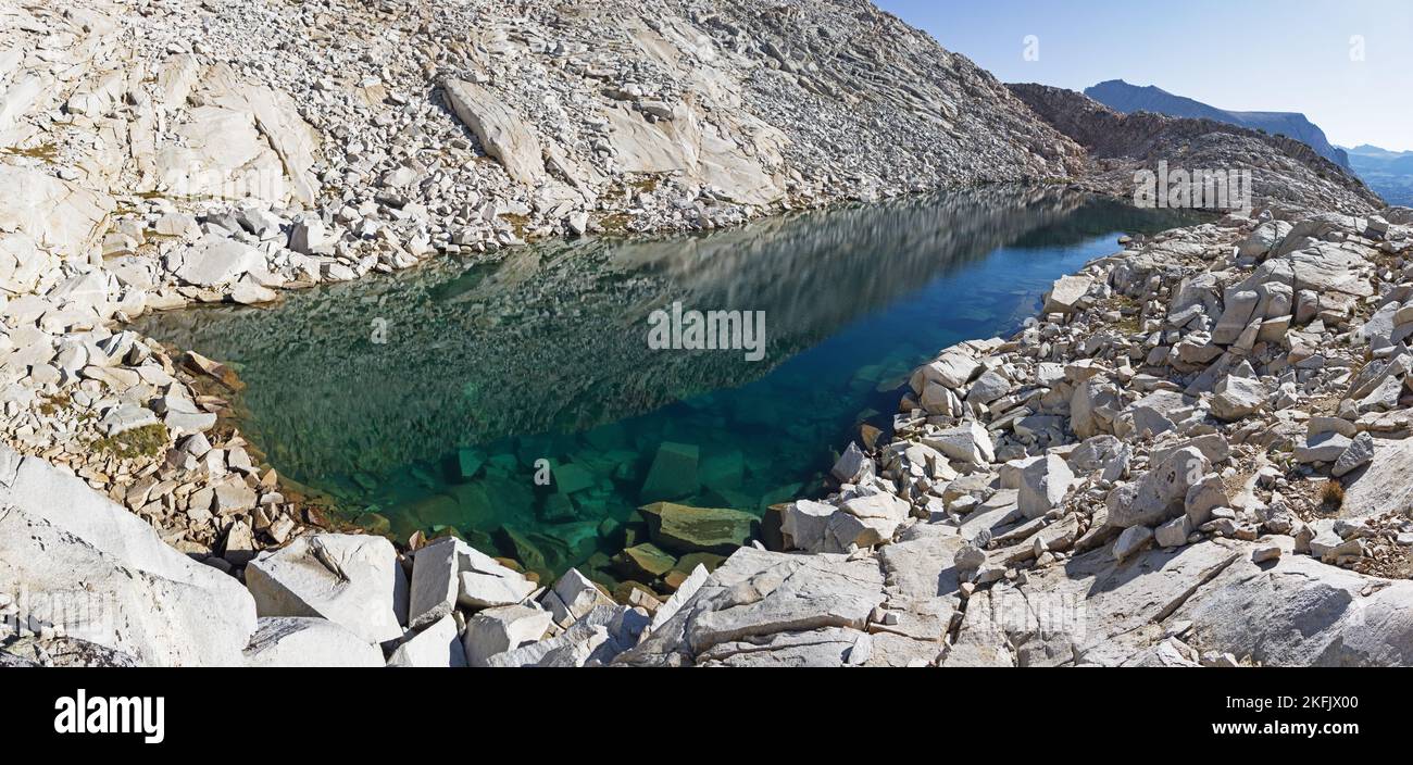 panoramic image of a clear blue mountain lake with boulders visible under the water Stock Photo