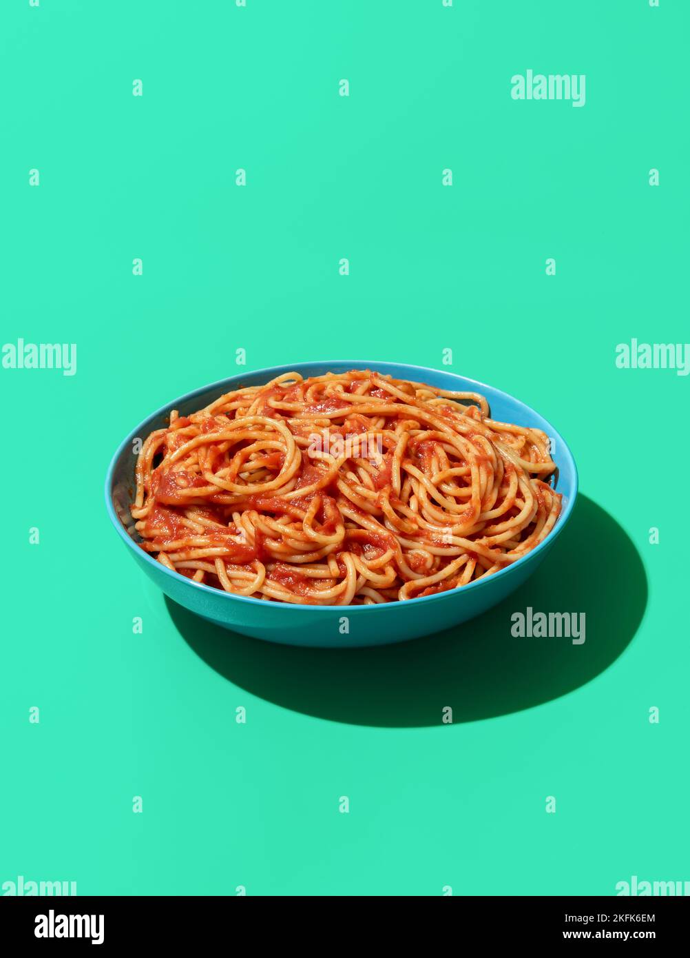 Bowl with spaghetti in tomato sauce minimalist on a green table. Pasta Pomodoro in a blue bowl in bright light on a green-colored background Stock Photo