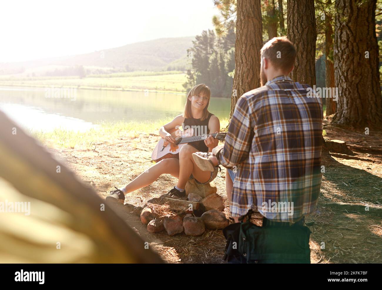 Music to my ears in the outdoors. a young woman playing guitar for her boyfriend at their campsite. Stock Photo