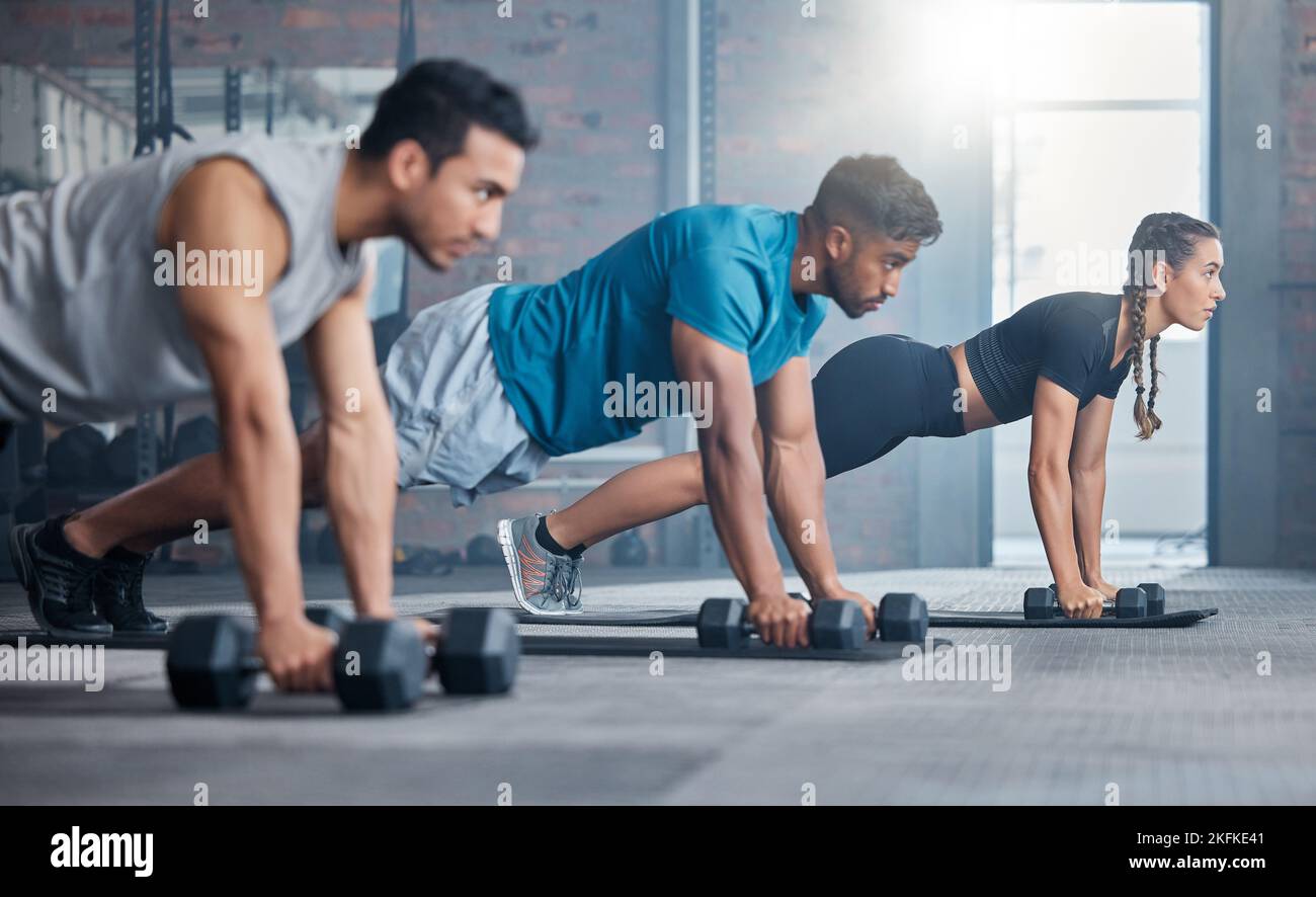 Group, workout and dumbbell push up at gym for muscle, power or strength. Teamwork, sports or energy of people, athletes or bodybuilder friends Stock Photo