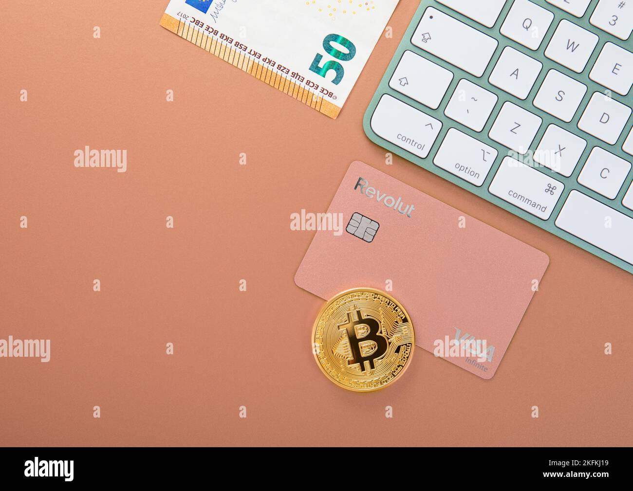LONDON,UK - NOVEMBER 12, 2022: Revolut visa card with bitcoin and keyboard on bronze background with fifty euro bill. Top view. Stock Photo