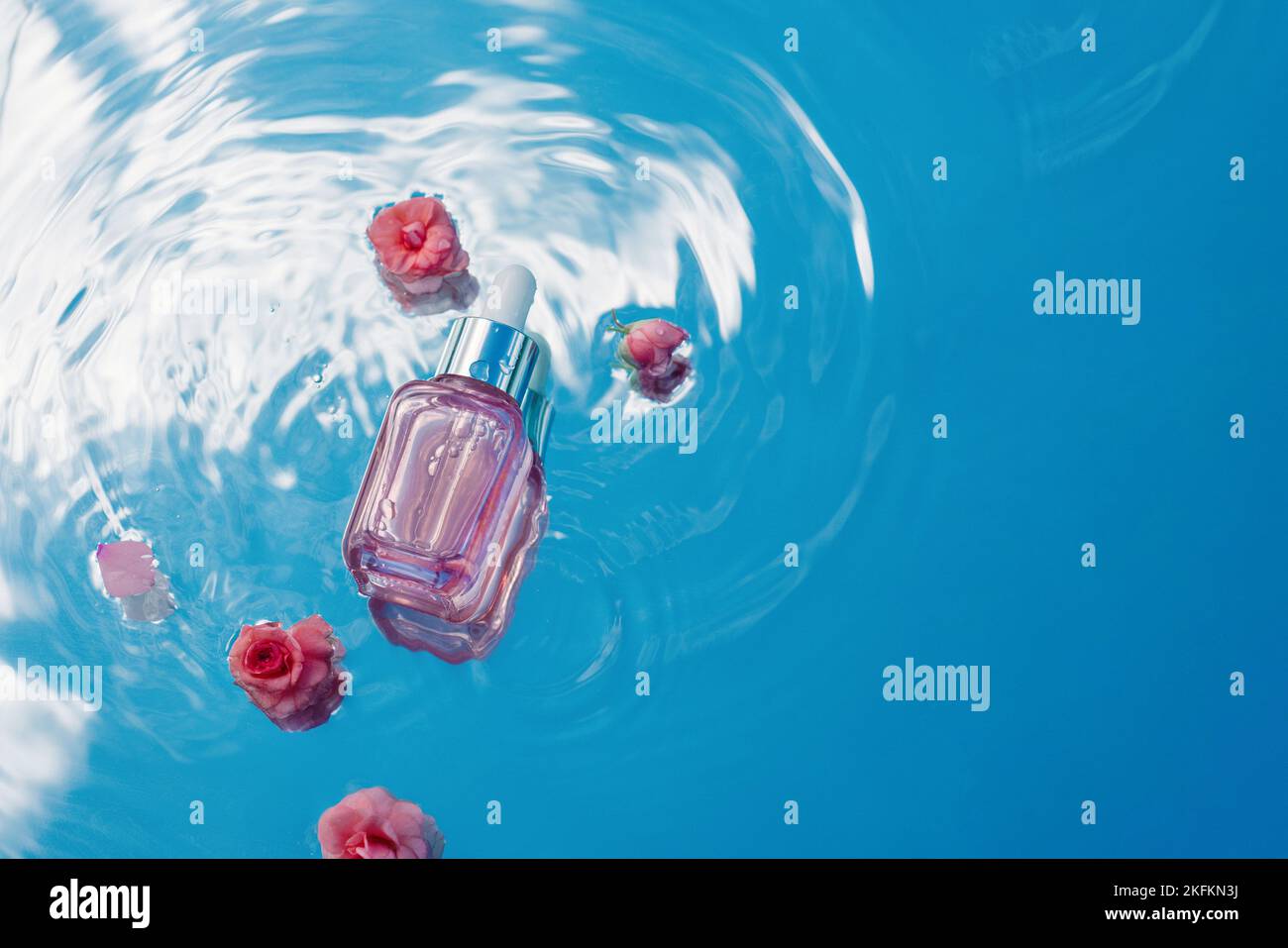 Blue water background with ripples and cosmetic bottle with pink roses