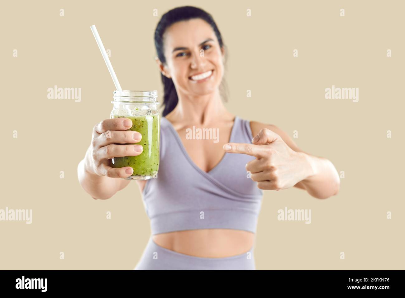 Caucasian woman holds out appetizing green smoothie, to maintain healthy food or vegetarian diet Stock Photo