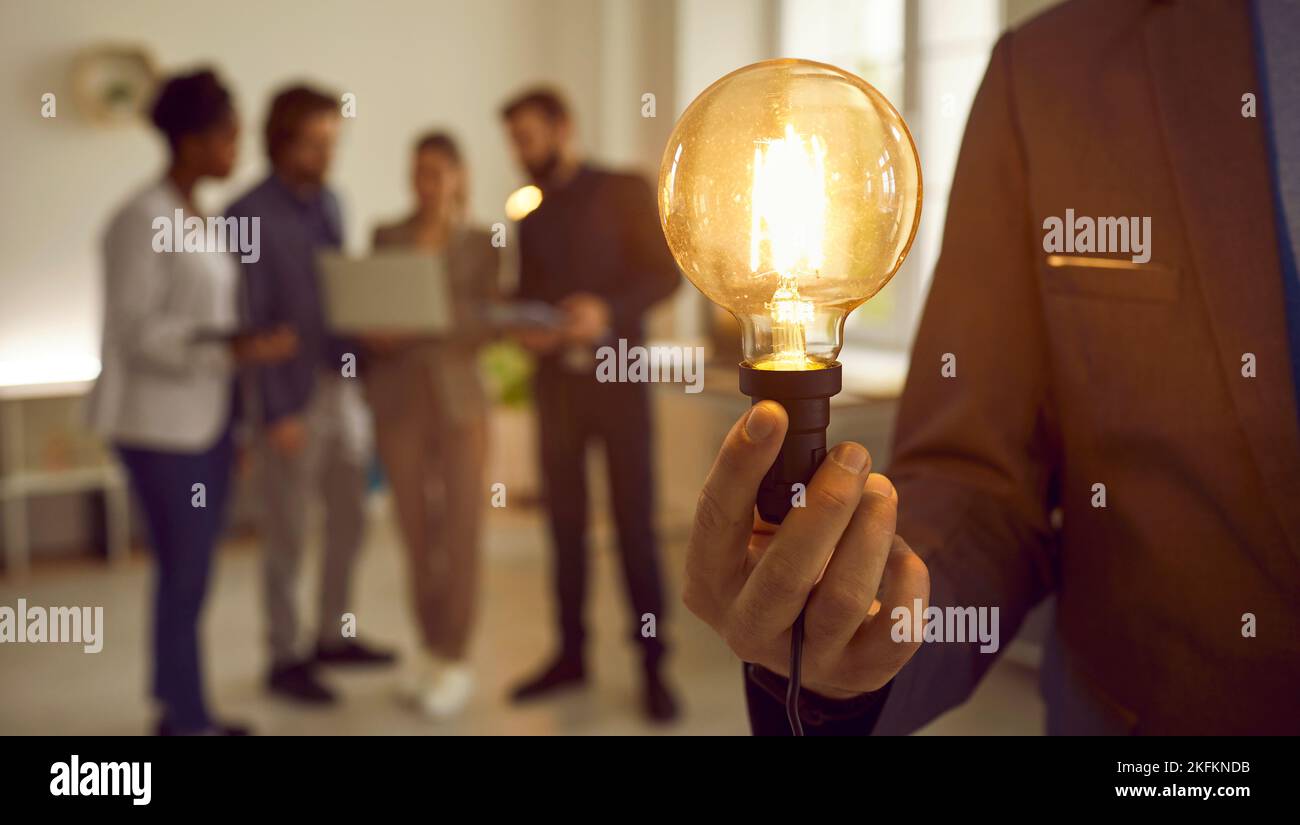 Man holding idea lightbulb in hand, with creative business team working in background Stock Photo