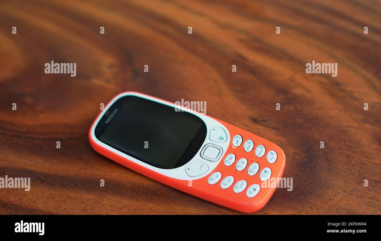 A keypad phone with buttons isolated on black background. Old Cell phone with black display. Closeup of a 2g, 3g orange mobile in India. Technology an Stock Photo