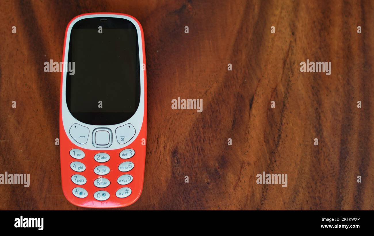 A keypad phone with buttons isolated on black background. Old Cell phone with black display. Closeup of a 2g, 3g orange mobile in India. Technology an Stock Photo
