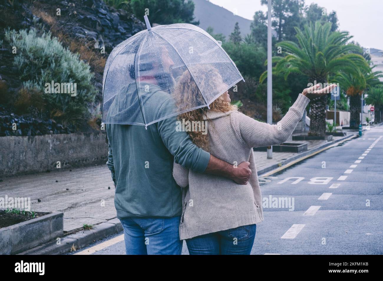 Back view of happy couple in love enjoying rain day with umbrella. Urban street in background. Outdoor leisure activity and concept of relationship to Stock Photo