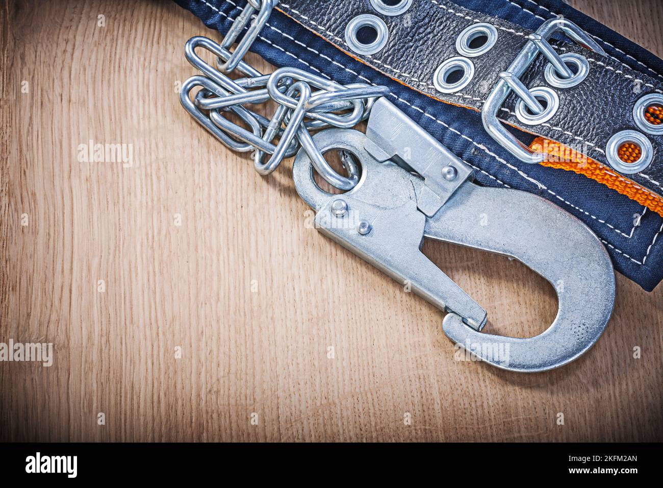 Construction body belt with metal carabiners chain on wooden board. Stock Photo