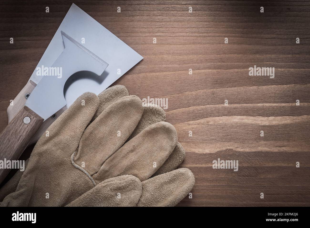 Construction safety gloves and putty knives on wooden background Stock