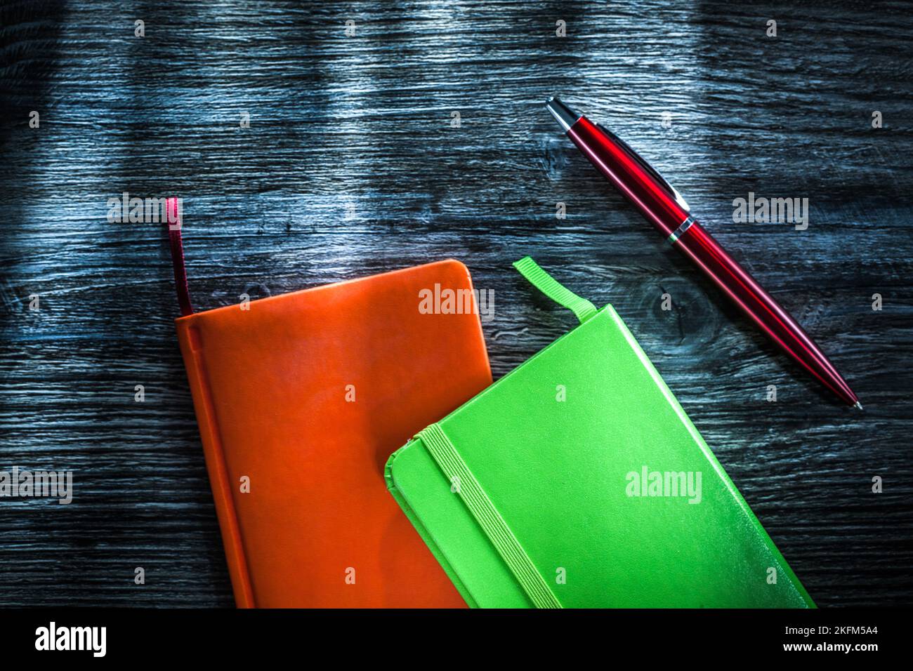 Green and orange notebooks on wooden board. Stock Photo