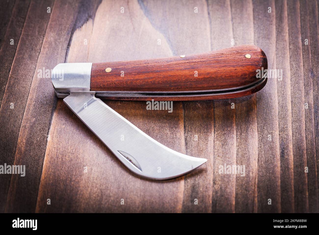 opened agricultural knife on vintage wooden board close up Stock Photo