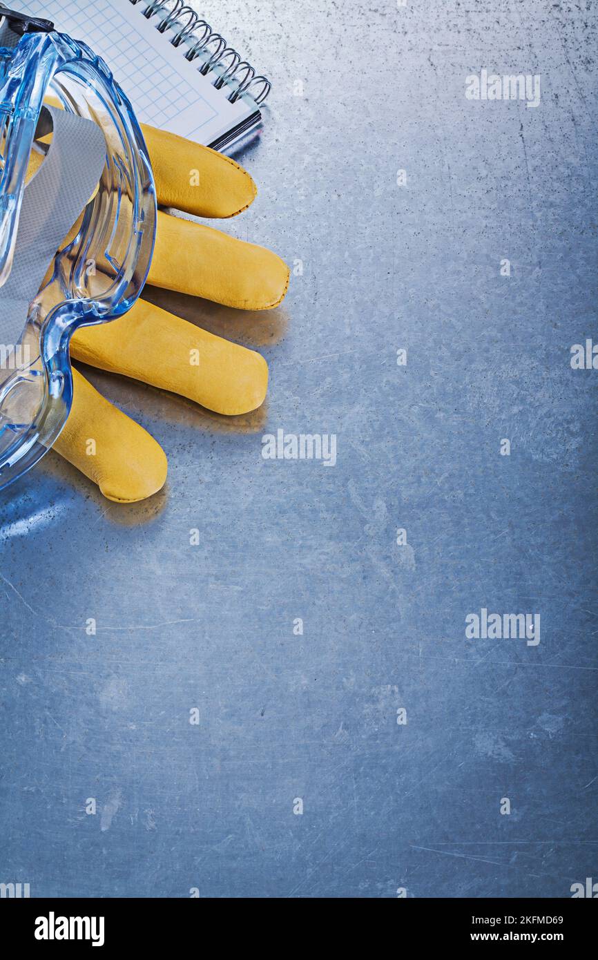 Safety spectacles leather gloves copybook on metallic background