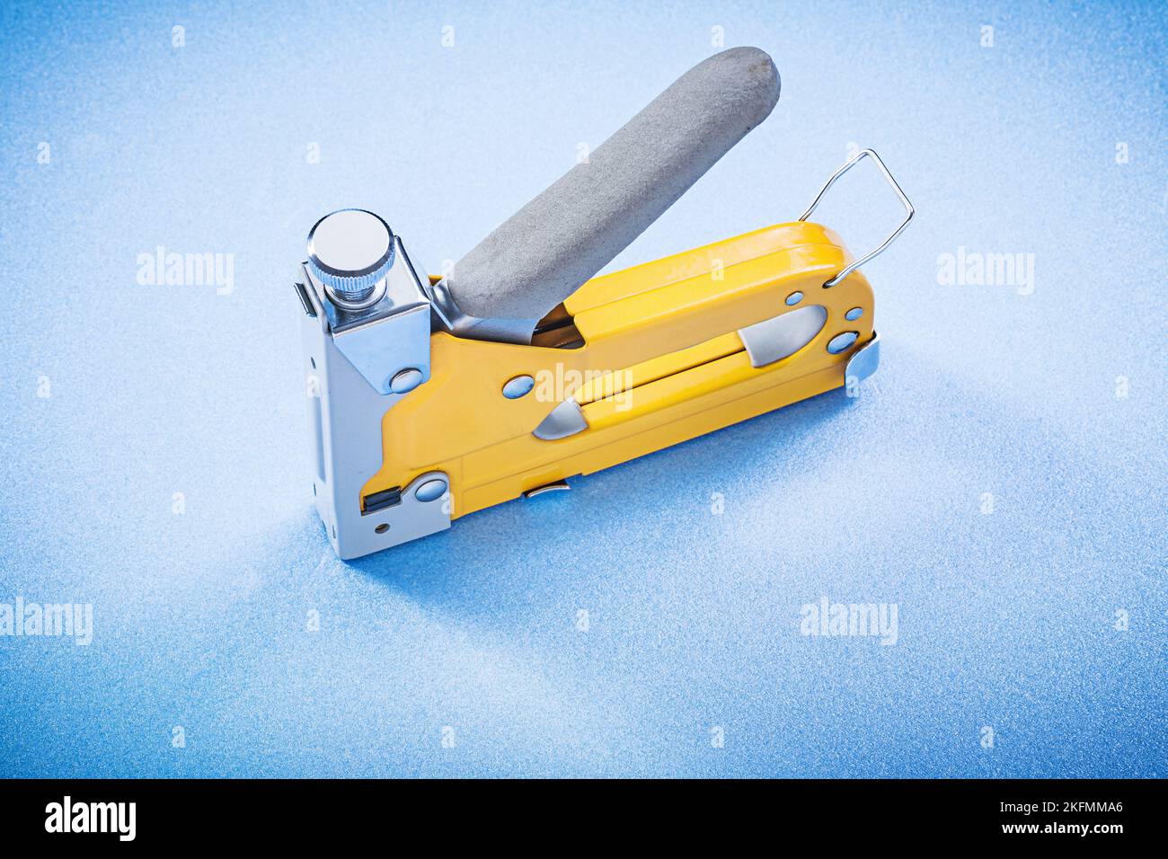 Yellow metal construction stapler on blue background top view. Stock Photo
