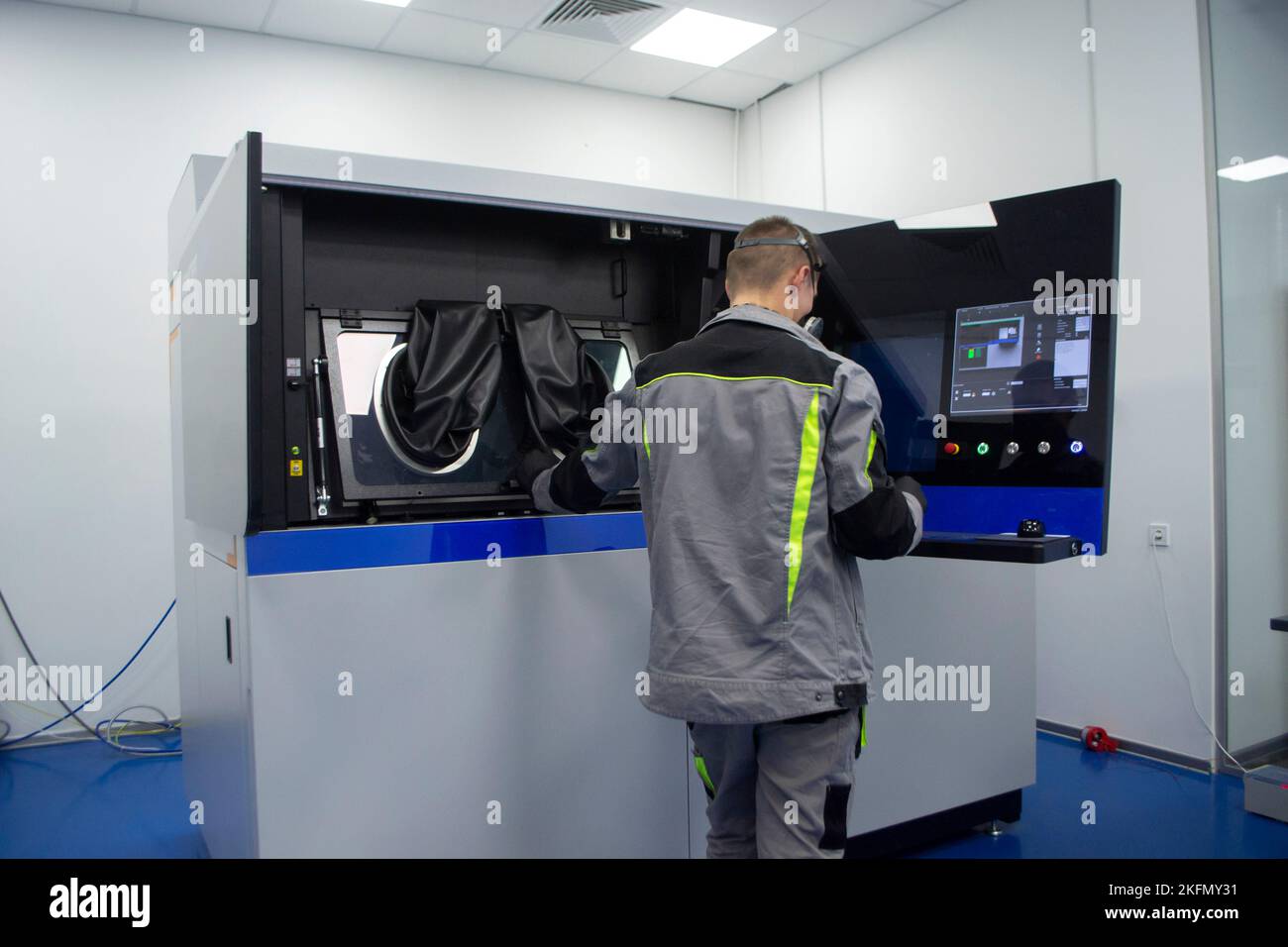 Industrial powder 3d printer for metal and worker man. Man in protective suit standing near