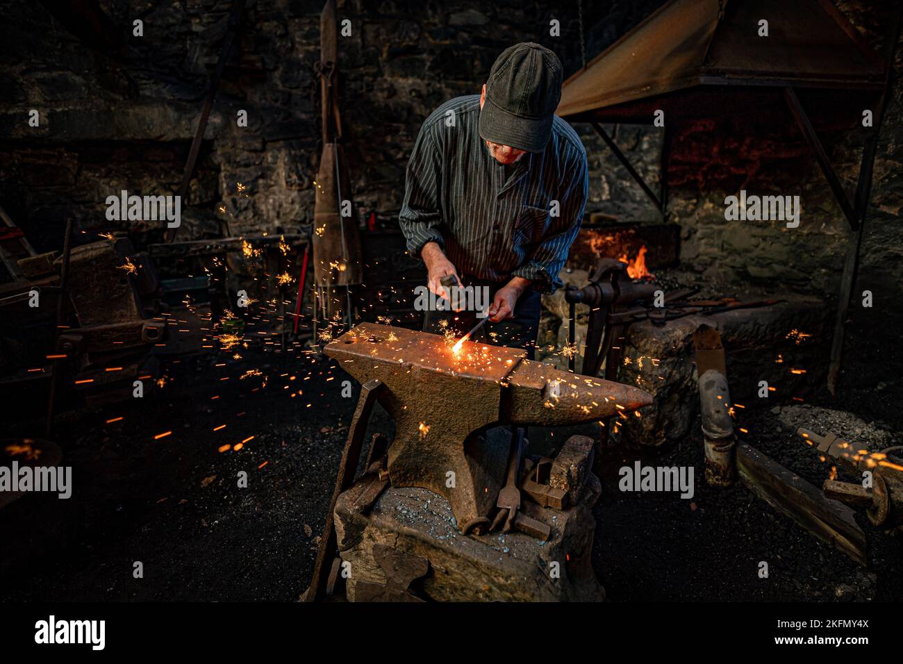Sparks fly as a blacksmith forges steel on an anvil at the National Trust's Finch Foundry in Oakhampton, Devon to mark St Clement's Day, the patron saint for blacksmiths. Picture date: Saturday November 19, 2022. Stock Photo