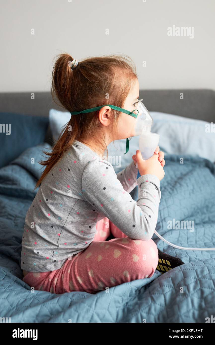 Sick little girl having medical inhalation treatment with nebuliser. Child with breathing mask on her face sitting in bed Stock Photo