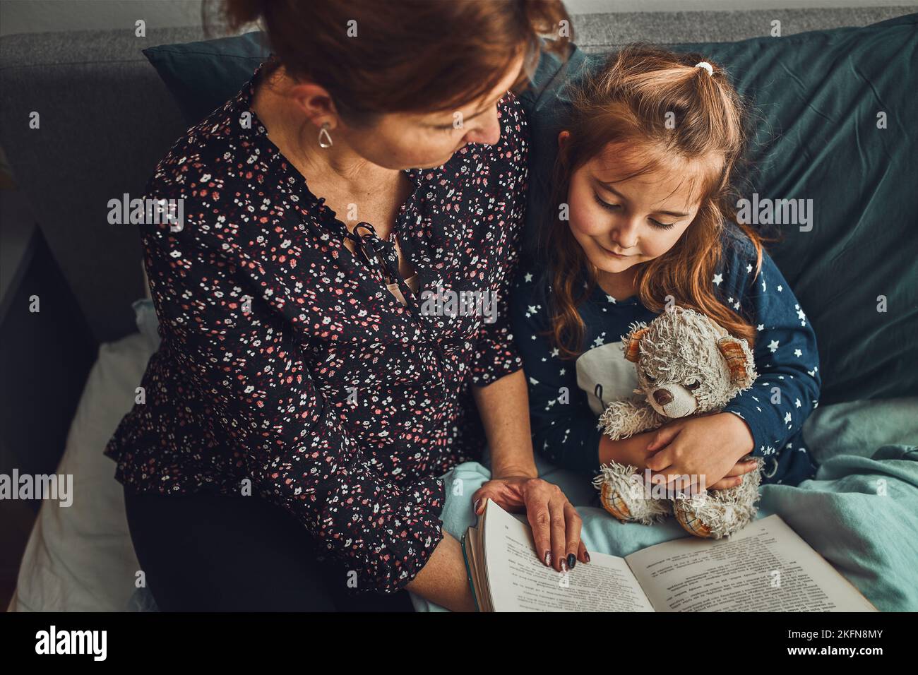 Mother reading book her daughter in bed before going to sleep. Reading