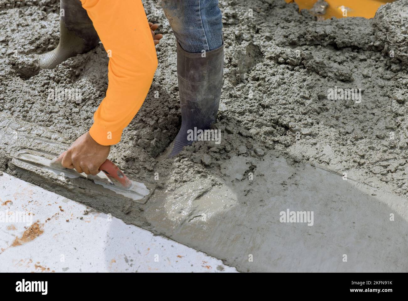 An employee is holding steel trowel as he smooths leveling over freshly poured concrete sidewalk in construction zone Stock Photo