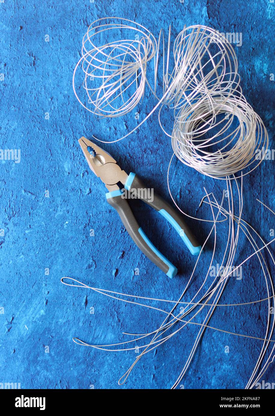 Vintage pliers, wire and reinforcement steel on blue textured background with copy space. House renovation work in details. Stock Photo