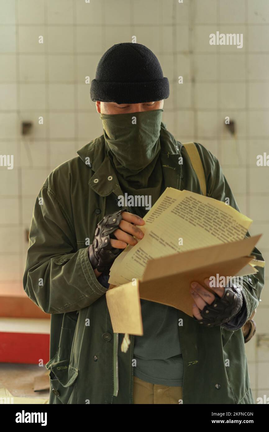 Disaster survivor soldier in a post apocalyptic world, he is wearing a bandana mask and reading documents. Environmental disaster and post-apocalyptic Stock Photo