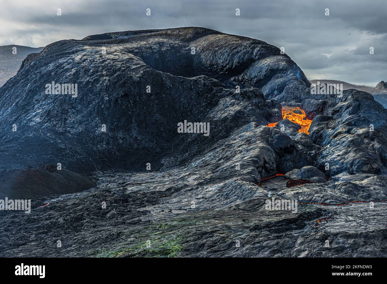 Opening of a volcanic crater during the day. crater with beginning lava flow. volcanic landscape on iceland of reykjanes peninsula. dark magma rock Stock Photo