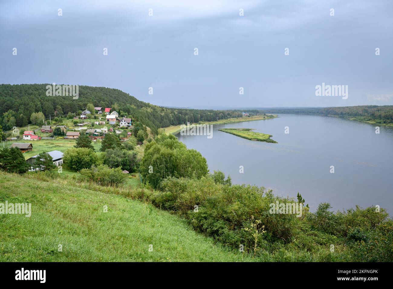 View of the Siberian Tom River with coastal meadows, forests and a village under a rainy sky Stock Photo