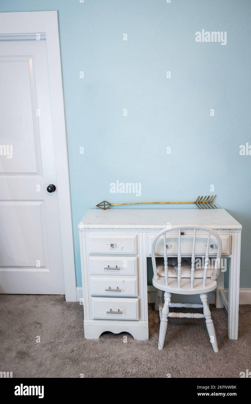 A small white child's desk and chair in a pale blue bedroom in a new