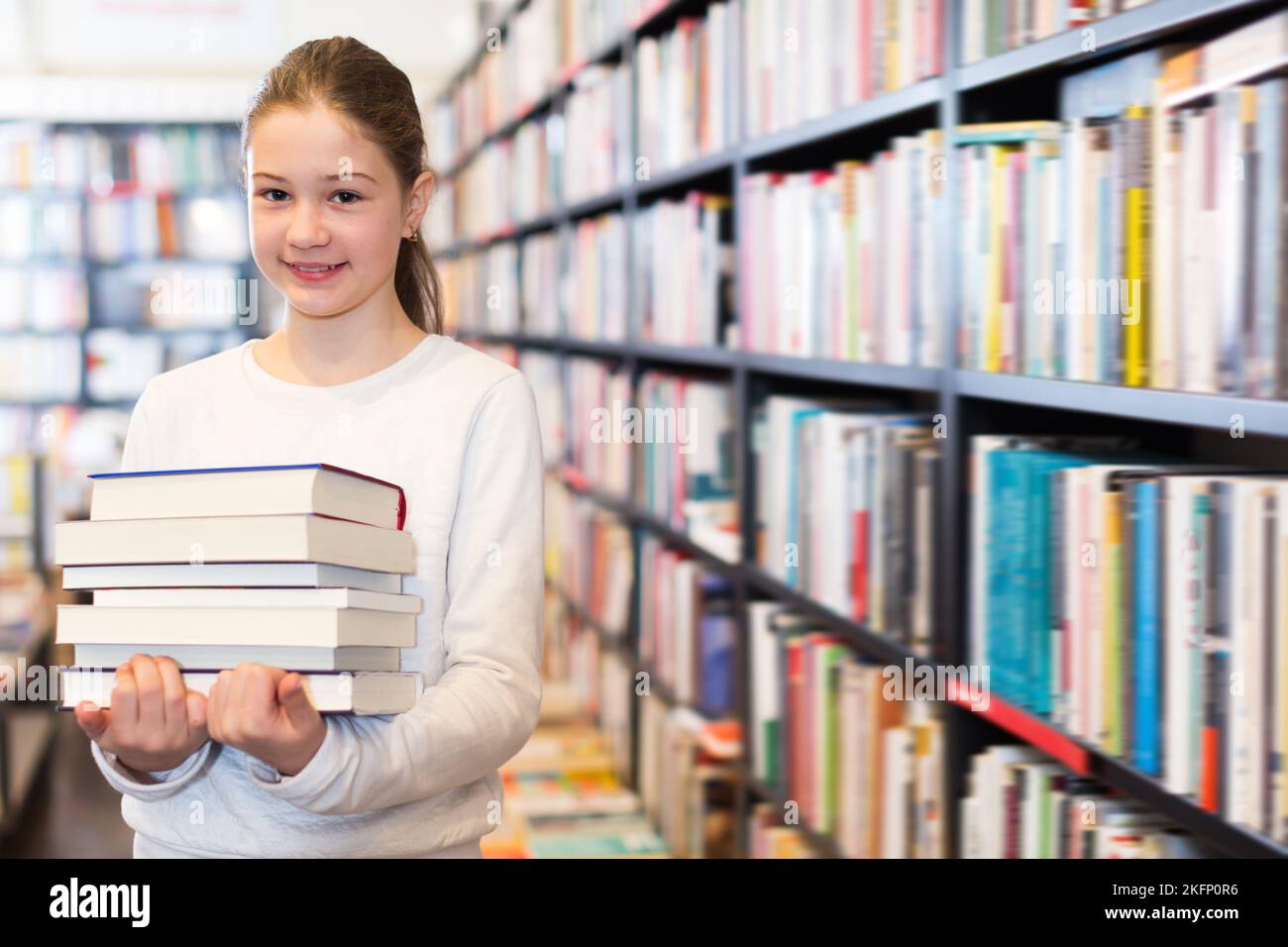 Smiling preteen girl holding stack of books Stock Photo - Alamy