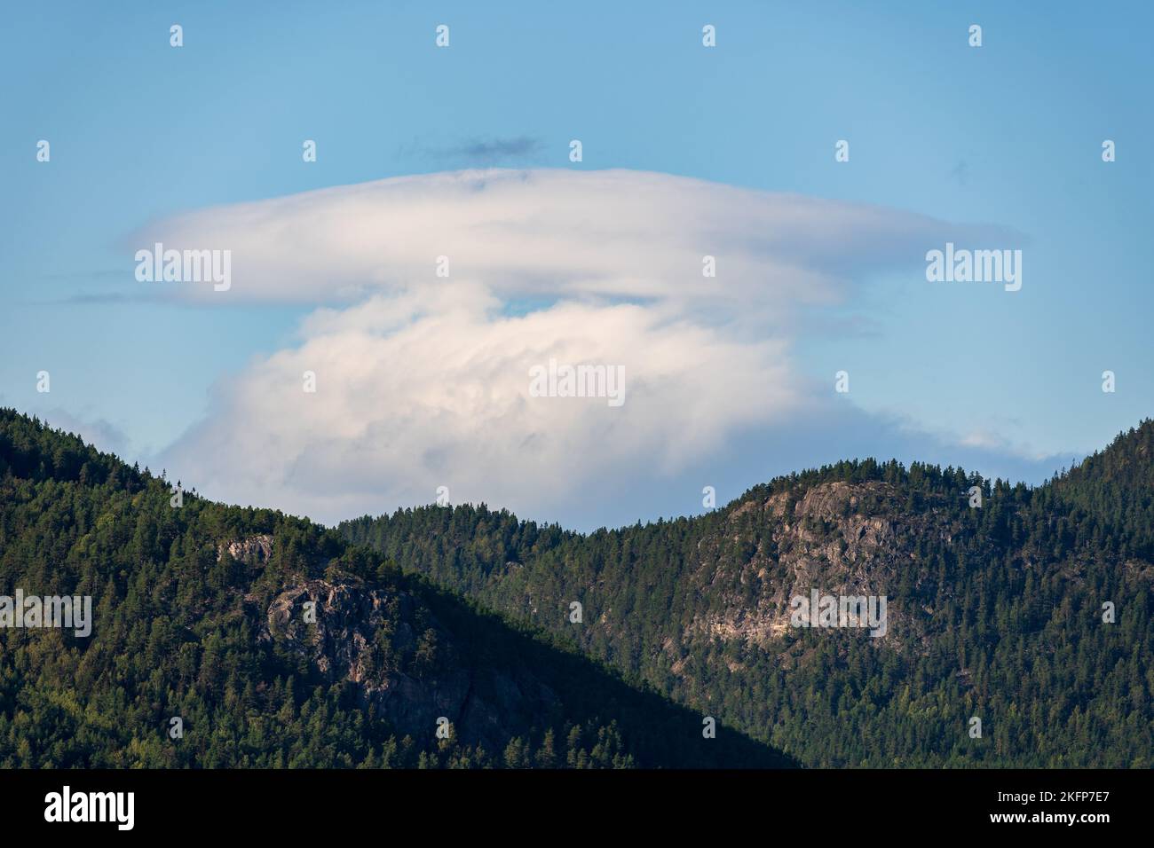 An anvil cloud formation over mountains covered in coniferous forests - cumulonimbus incus Stock Photo