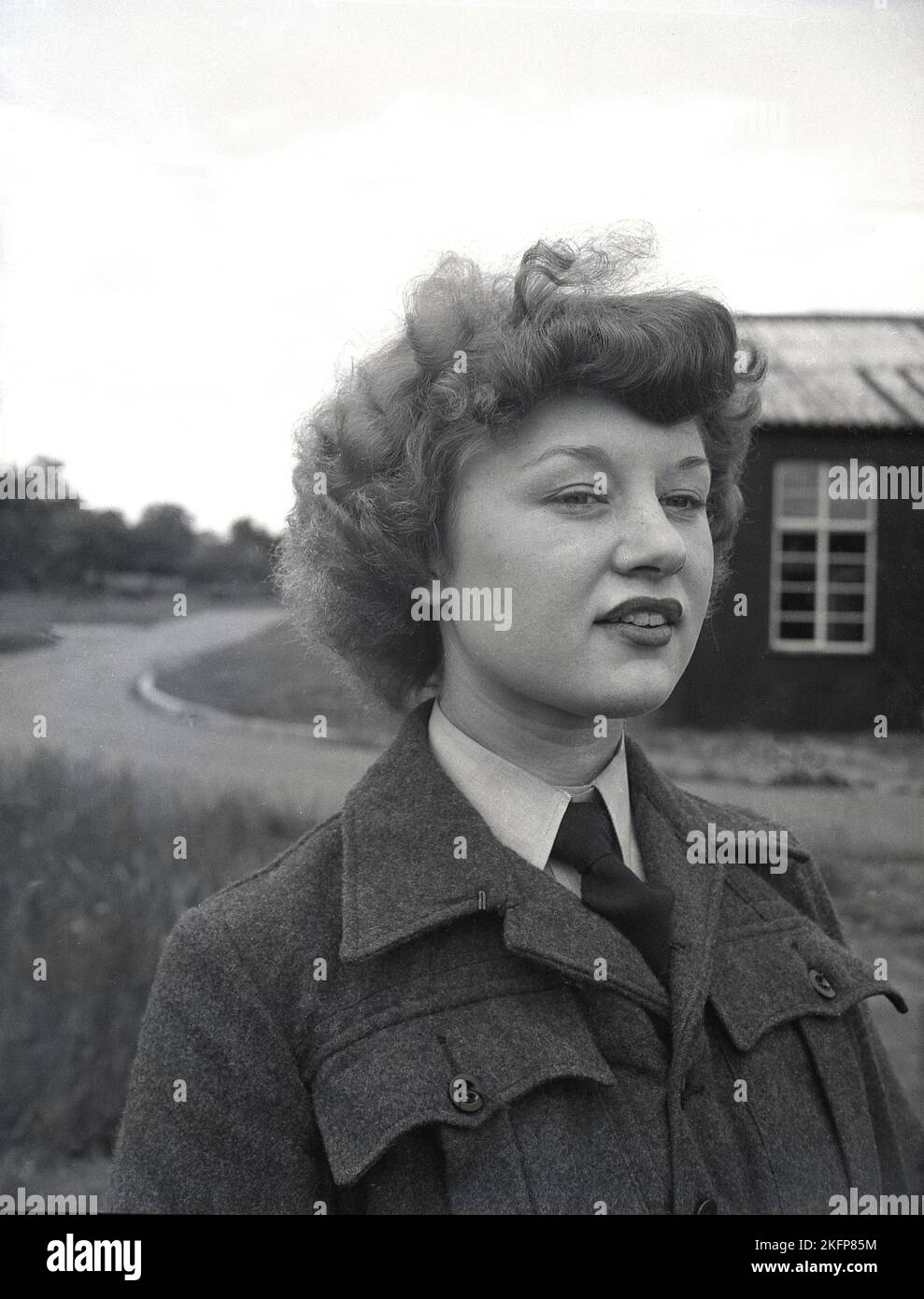 1940s, historical, standing outside the camp, at RAF Ternhill, Longford Camp, near Market Drayton, Shropshire, England, UK, a young female WAAF in a collar and tie and woollen cloth tunic. The Women's Auxillary Air Force (WAAF) was formed in June 1939, with intital recruits being between 18-43 years old. Stock Photo