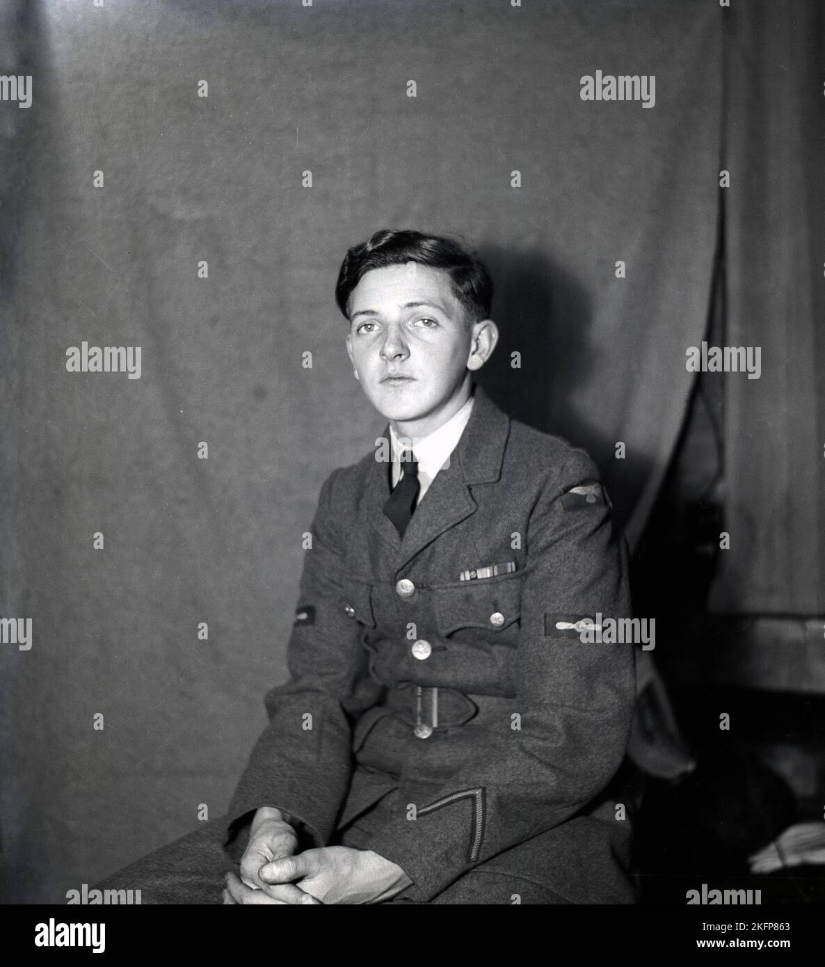 circa 1949, historical, at RAF Ternhill, Market Drayton, Shropshire, England, UK, a young man, a Junior NCO sitting inside for his photo. His service dress or uniform is made from Barathea, a traditional worsted wool fabric, smoother than an airman's heavy and thick wool uniform.  On the lower left arm of his tunic, a points-up chevron insignia, which was an RAF Good Conduct Stripe, in the middle of the tunic, just above the elbow, a propeller emblem, denoting a Leading Aircraftman and on the upper arm, an RAF Shoulder Flash. Stock Photo